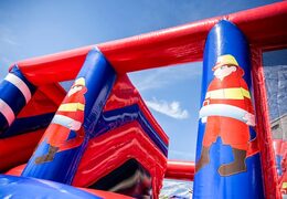 Inflatable covered bounce house in the theme of a fire department with a slide on the jumping surface, climbing tower and fun obstacles for kids. Buy bounce houses online at JB Inflatables UK